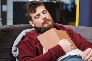 本を持ったままソファで眠る男性の写真